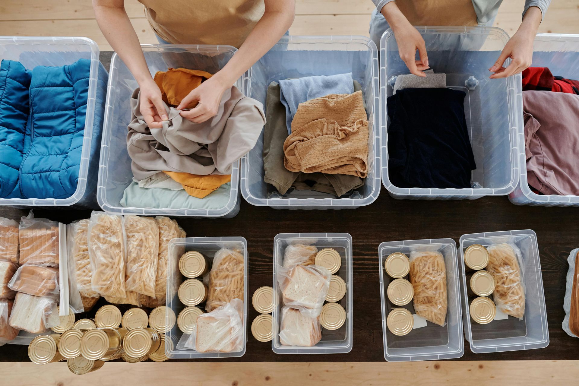 People sorting clothes and food items into clear bins on a wooden table.