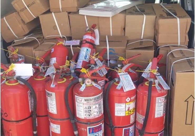 Varios extintores rojos apilados delante de cajas de cartón en una zona de almacenamiento.