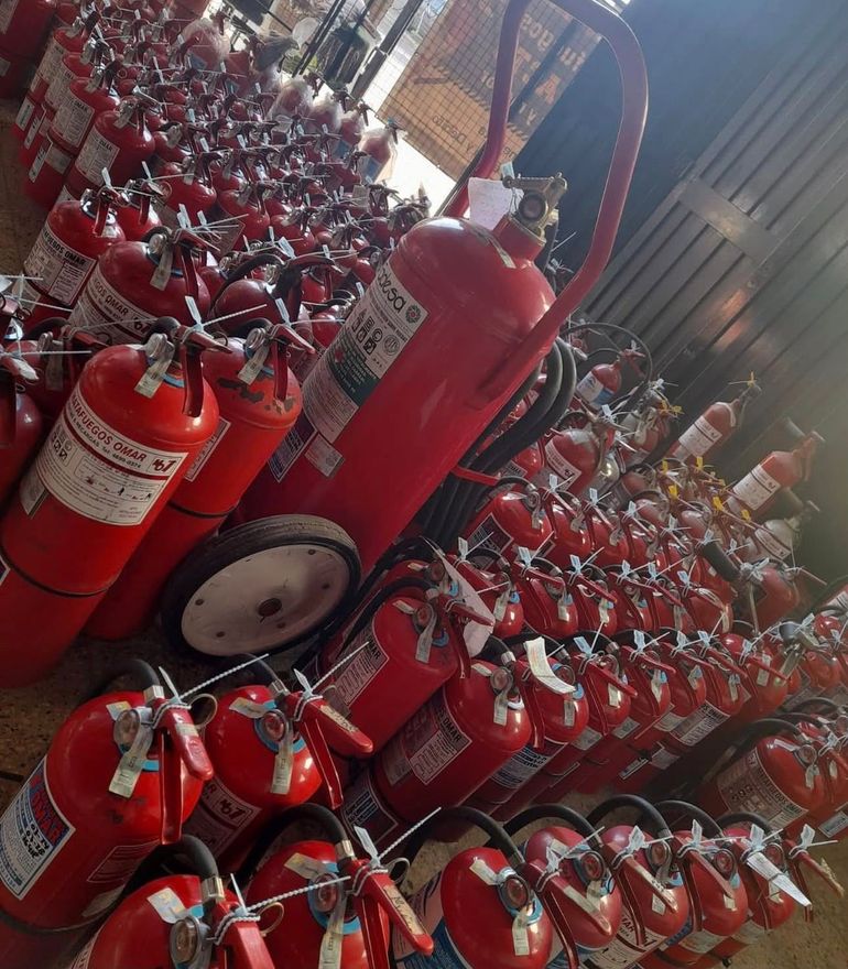 Filas de extintores rojos apilados en una zona de almacenamiento, con un extintor grande en primer plano.
