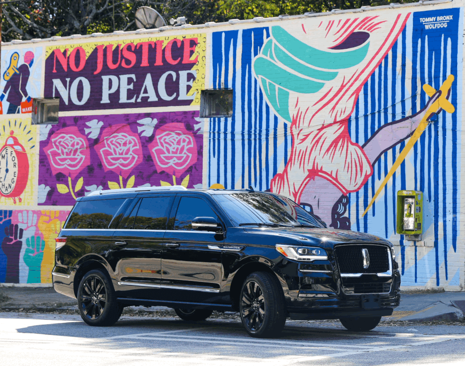 A black suv is parked in front of a mural that says no justice no peace.