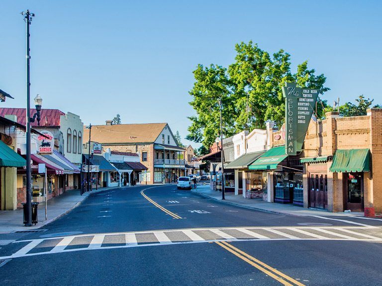Street lined with shops and businesses on a sunny day; crosswalk in the foreground.