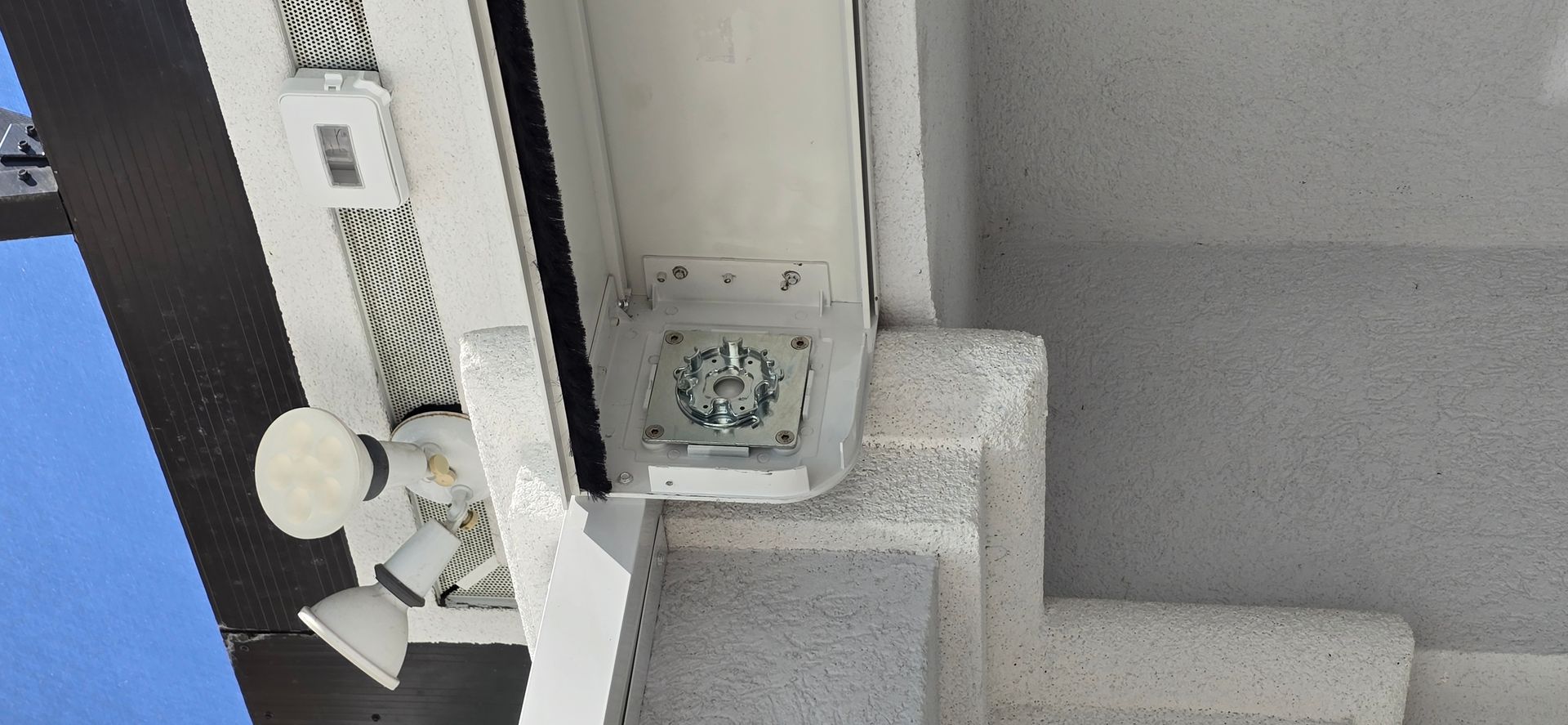 White flood lights and mounting hardware on a textured white exterior wall.
