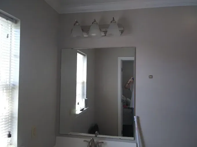 Bathroom with mirror, lights, window, and cabinet; walls are painted light grey.