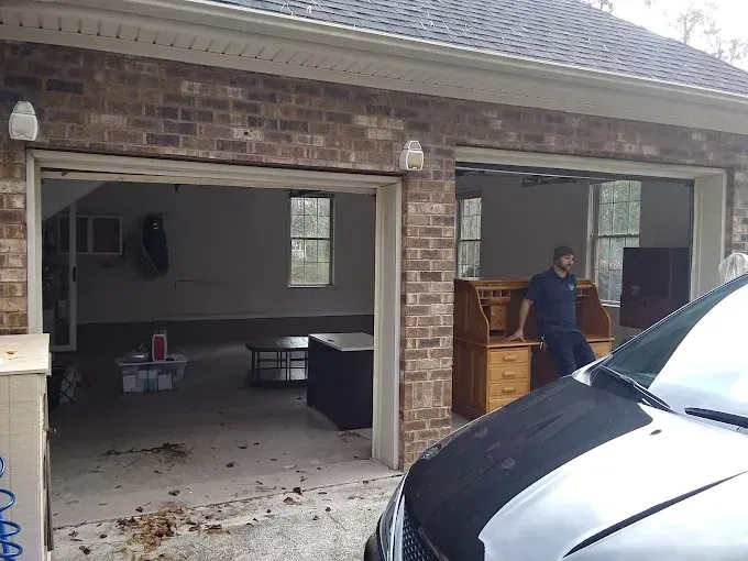 Garage with open doors, partially filled with furniture. A person stands near a desk.