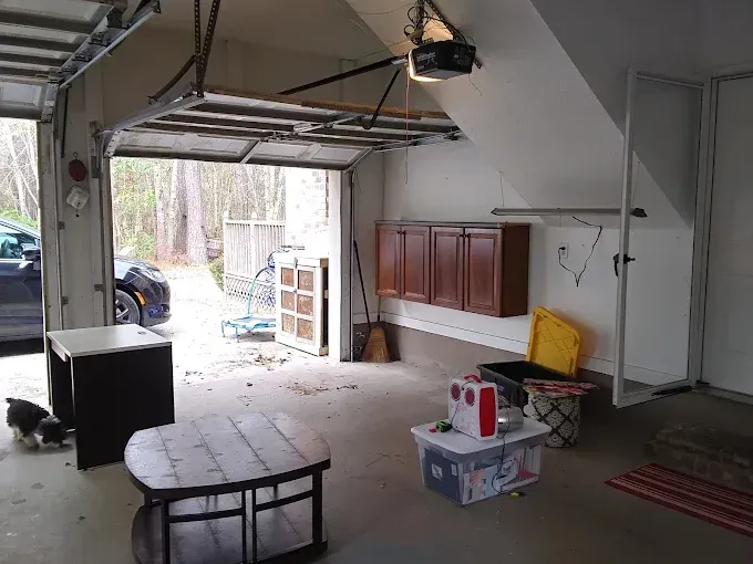 Garage interior with open door, car visible, storage cabinets, furniture, and a dog.