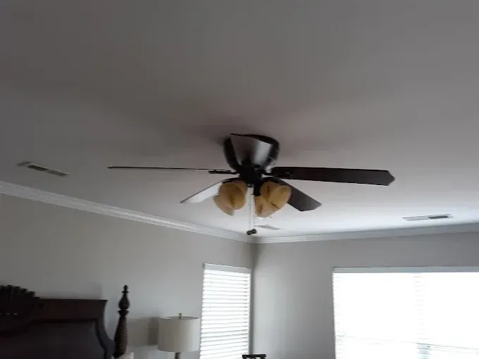 Ceiling fan with lights in a bedroom. Brown blades, white walls, and a window.