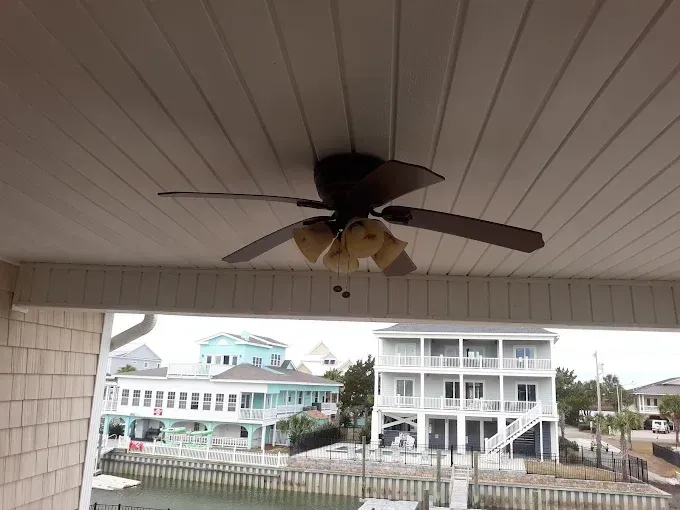 Ceiling fan on a white porch, overlooking waterfront homes.
