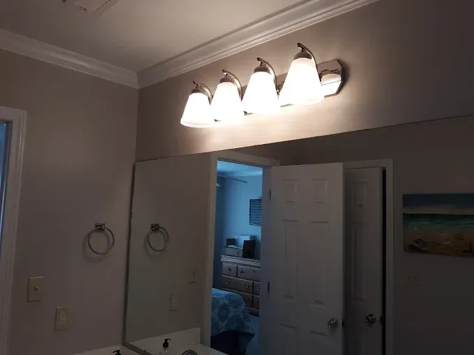 Bathroom with mirror, four-bulb light fixture, white doors, and a partial view of another room.