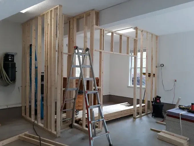 Wooden framing for interior walls in a garage, with a ladder in front and a window visible.