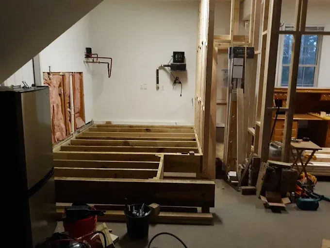 Interior construction site with wooden framing, electrical and plumbing fixtures, and exposed insulation.