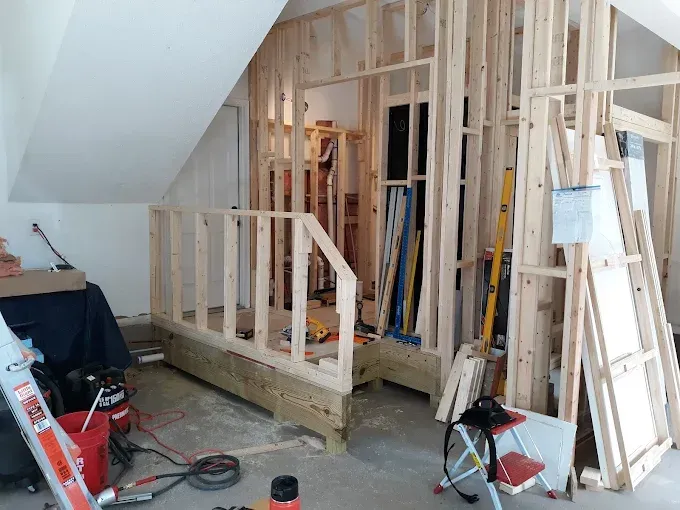 Interior framing of a room under construction with studs, a railing, and a sloped ceiling.