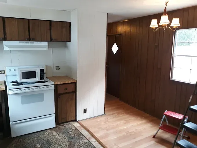 Kitchen and dining area with white appliances, brown cabinets and paneling, and a chandelier.