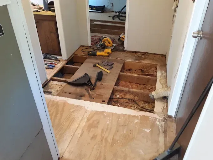Hallway undergoing renovation with exposed floor joists, tools, and partially removed flooring.