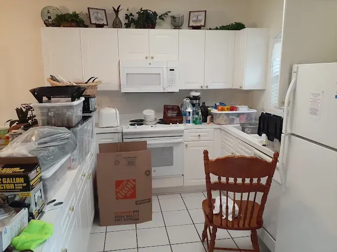 White kitchen with upper and lower cabinets, appliances, and a wooden chair.