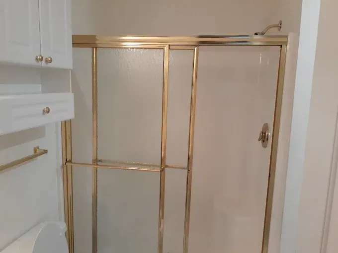 Shower stall with gold-colored frame and sliding doors. White walls and adjacent white cabinetry.