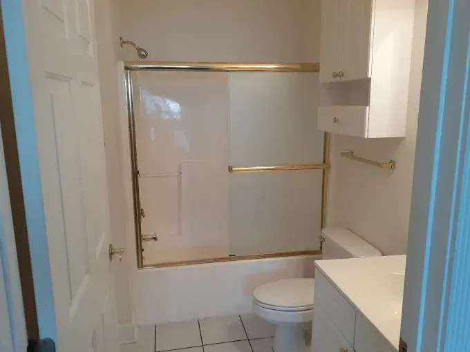 Bathroom with white fixtures, a gold-framed shower, and a cabinet above the toilet.
