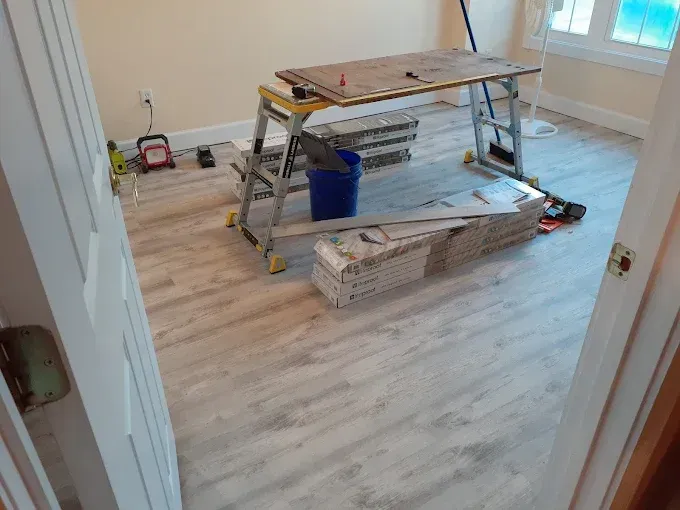 Room with new wood-look flooring being installed; work table, buckets, and tools are in the room.