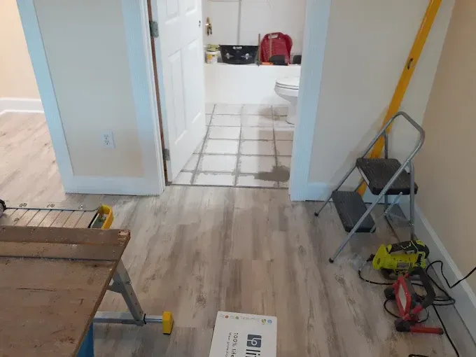 Bathroom floor renovation with new flooring installed. Doorway with a level, step stool, and tools.