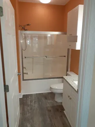 Bathroom with orange wall, white fixtures, gray floor, and sliding glass shower doors.