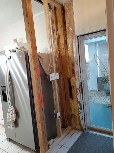 Interior wall with exposed studs, electrical wiring, and a doorway. Refrigerator on the left.