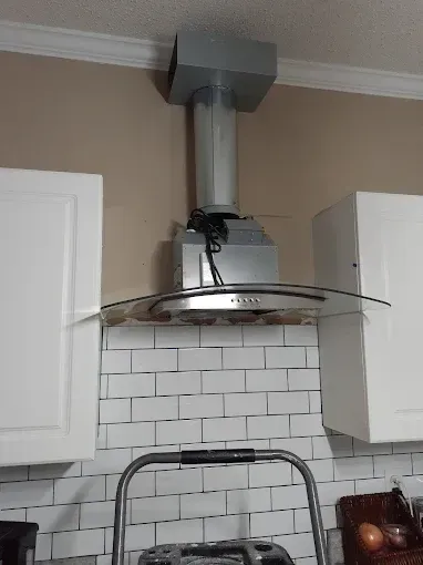 Range hood installed between white cabinets, over subway tile backsplash, with a ladder in front.