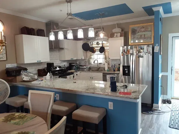 Kitchen with white cabinets, island with stools, stainless steel appliances, and blue accents.