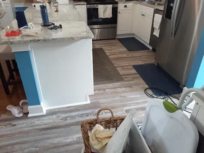 Kitchen with island, stainless steel appliances, and wood-look flooring. White cabinets, blue accent, and basket visible.