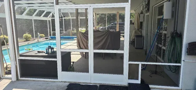 A screened patio with a pool in the background. The doors are open leading to an outdoor seating area.