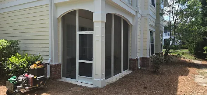 Screened-in porch on a multi-story building. Beige siding, white trim, and a brick base.