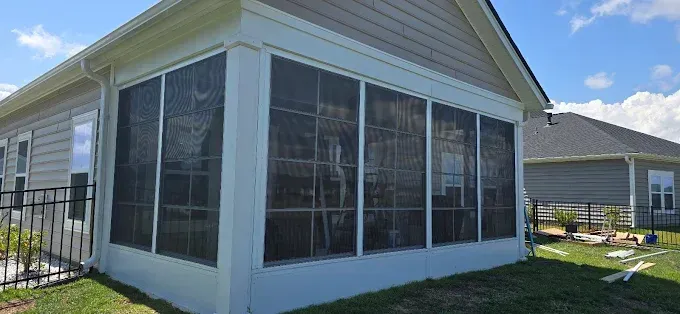 Screened-in porch attached to a house with a blue sky background.