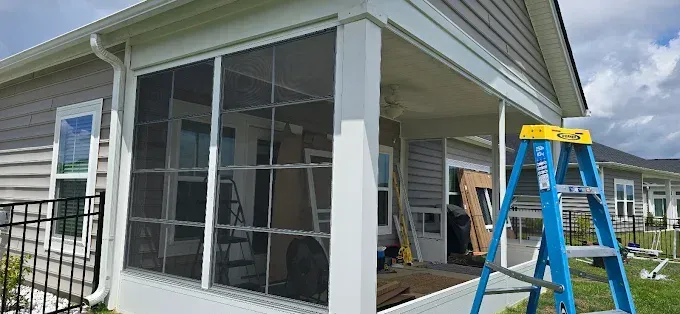 Screened porch with blue ladder leaning against it. House exterior visible.