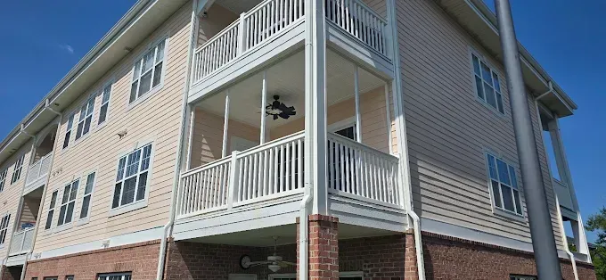 Multi-story building with white balconies and brick base against a blue sky.