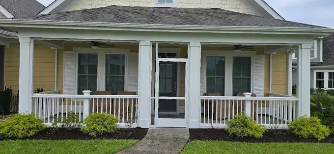 A yellow house with a white porch and screen door; green bushes and grass in front.