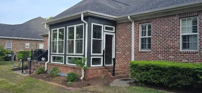 Exterior view of a brick house with a screened porch and green yard.