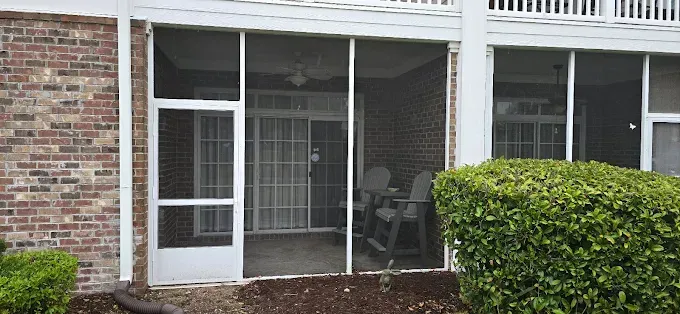 Exterior of a brick building with screened-in patio. Sliding glass doors lead to a furnished patio space.