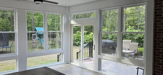 Sunroom interior with large windows overlooking a backyard with a swing set and patio furniture.