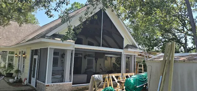 Screened porch addition to a house; outdoor view with building materials and trees.