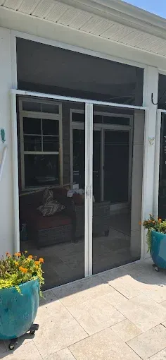 Screened patio door flanked by turquoise flowerpots on a paved surface.