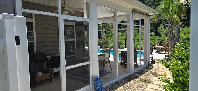Screened-in porch overlooking a pool and yard with stone path and lush greenery.