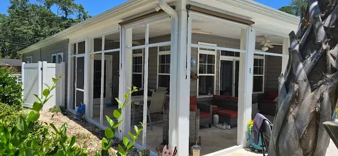 A screened-in porch with outdoor furniture; a fence and foliage are in the foreground.