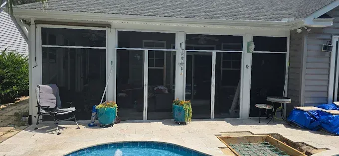A screened-in porch next to a pool. There are two blue planters, a chair, and a table.