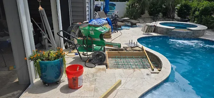 Poolside construction: Pool, hot tub, concrete, green concrete mixer, and red bucket.