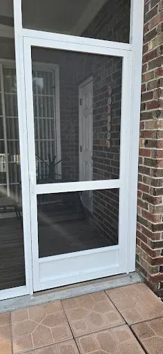 White-framed screen door on a brick building with a view of a second door and a patio.