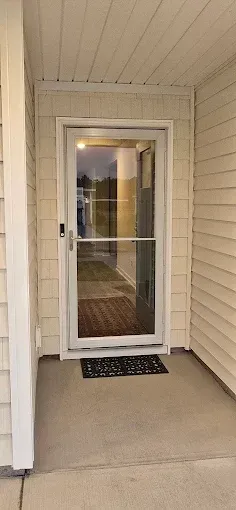 A glass door with a screen, on a porch. A welcome mat is at the bottom of the door. Beige siding surrounds the door.