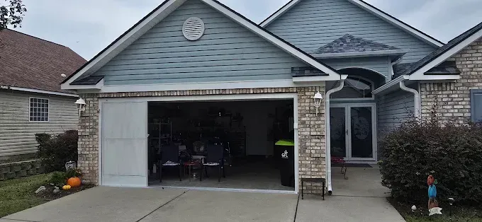 A house with an open garage, blue siding, and a tan brick facade.