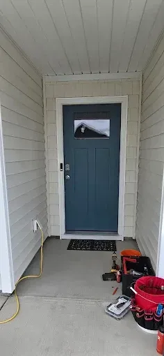 Blue front door with window, white trim, siding, and ceiling. Tools and a welcome mat on the porch.
