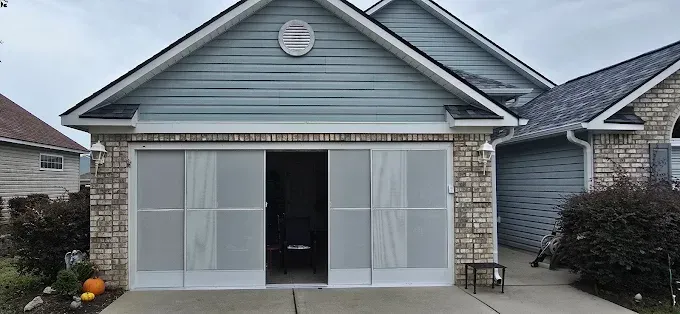 Garage with a blue siding exterior, open with screen doors. Brick facade on the sides and gray pavement.