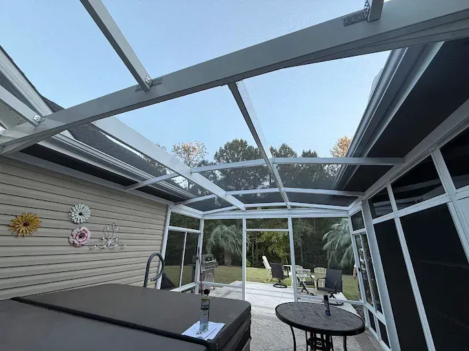 Sunroom interior with transparent roof and screened walls, overlooking a backyard.