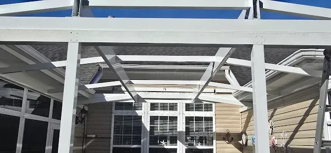 White screened-in patio with view of house windows and blue sky.