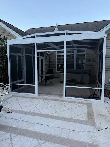 White screened-in patio with open doorways, concrete patio, and visible outdoor furniture.